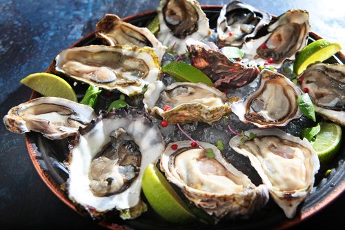 Fresh oysters with lime on a round plate. Oyster season. Macro-seafood dish. Oyster on the half shell.Two varieties of oysters.Out of focus.