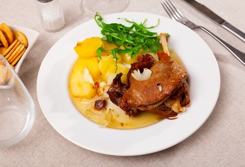 Confit de canard, roasted tasty duck confit with stew potatoes and arugula on a ceramic plate