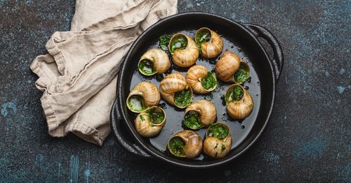 Escargots de Bourgogne Cooked Snails with Garlic Butter and Parsley in black cast iron pan on rustic stone background from above, traditional French Delicacy .